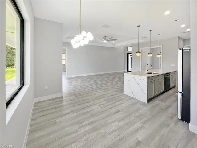 Kitchen featuring open floor plan, a raised ceiling, a center island with sink, light stone countertops, and freestanding refrigerator