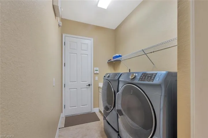 Washroom featuring a textured wall, washer and clothes dryer, and light tile patterned floors