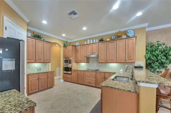 Kitchen with a peninsula, appliances with stainless steel finishes, dark stone counters, arched walkways, and crown molding