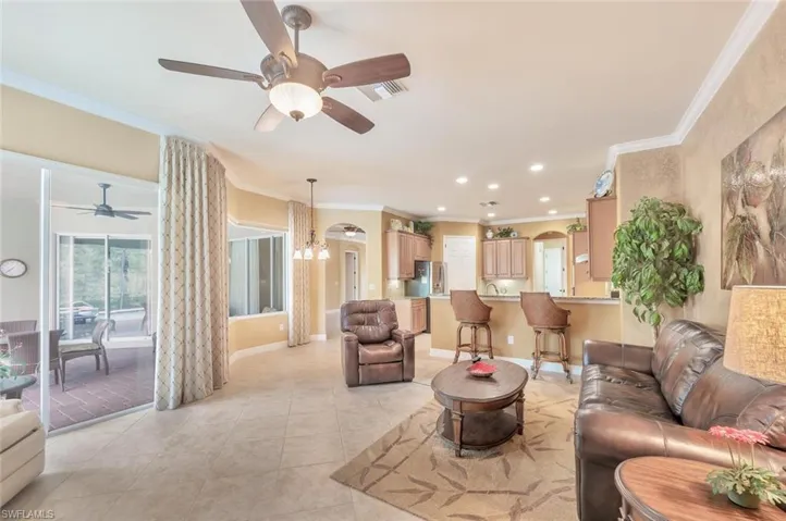 Living room featuring crown molding, arched walkways, ceiling fan, light tile patterned floors, and a chandelier