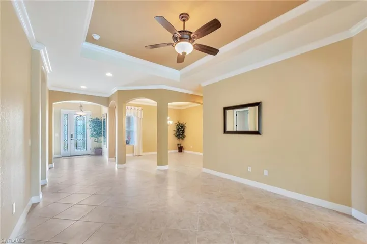 Empty room with arched walkways, a raised ceiling, ornamental molding, light tile patterned floors, and ceiling fan