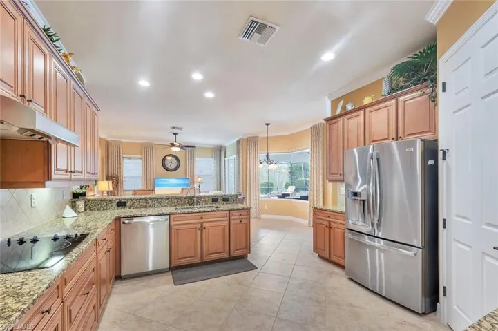 Kitchen with stainless steel appliances, crown molding, light stone countertops, hanging light fixtures, and a peninsula