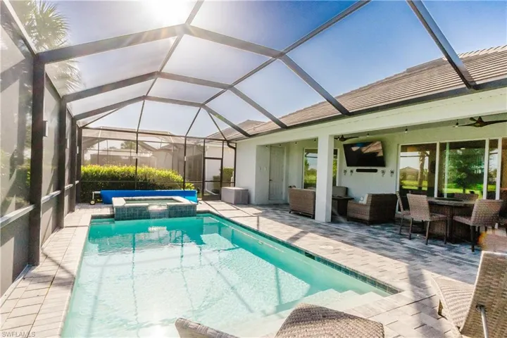 Screened outdoor living space featuring an inground pool, integrated spa, and paver decking