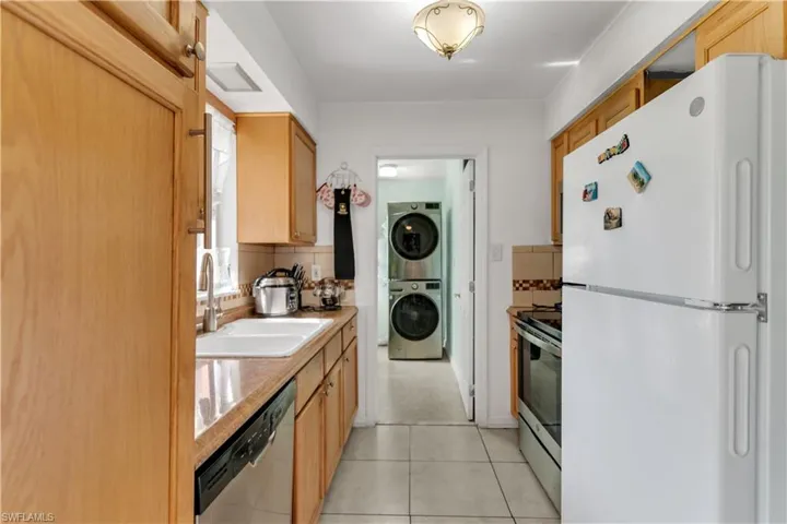 Kitchen with sink, decorative backsplash, light  patterned flooring, stacked washer / dryer, and stainless steel appliances