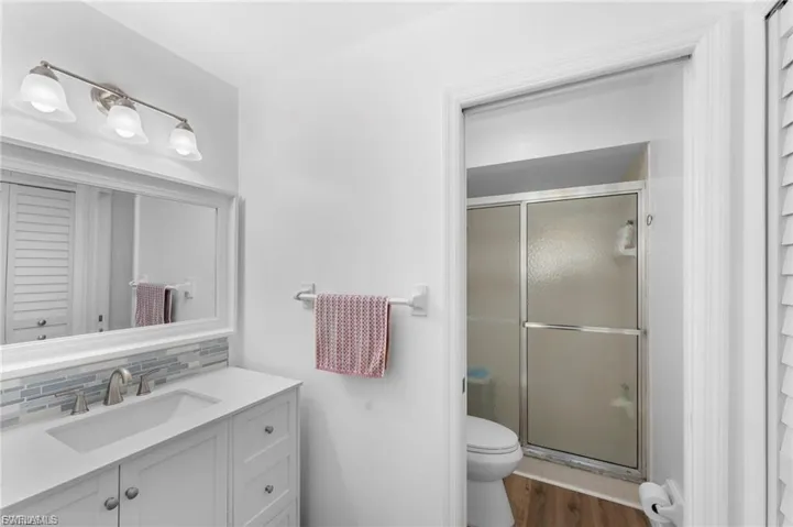 Primary bath with a stall shower, vanity, dark wood-type flooring, and backsplash
