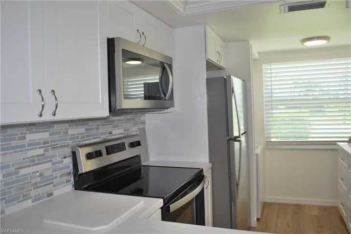 Kitchen featuring white cabinets, stainless steel appliances, decorative backsplash, and wood finished floors