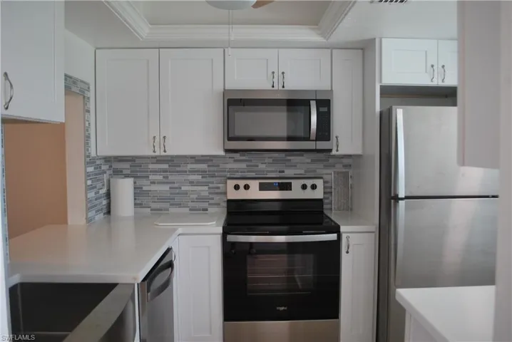 Kitchen featuring appliances with stainless steel finishes, white cabinetry, backsplash, crown molding, and light stone counters