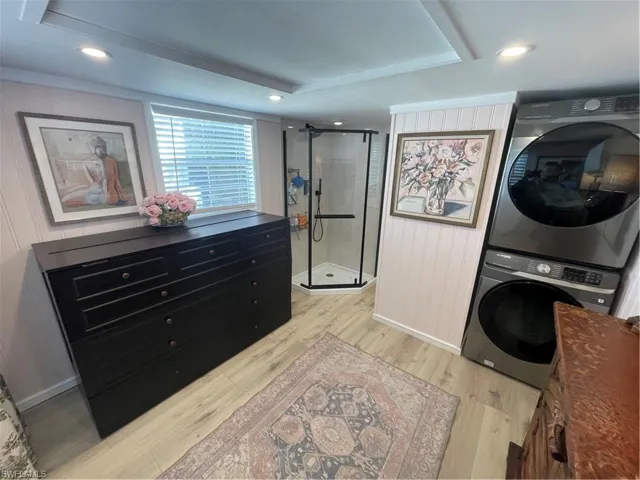 Laundry area featuring stacked washer / dryer, light wood-type flooring, recessed lighting, and wooden walls