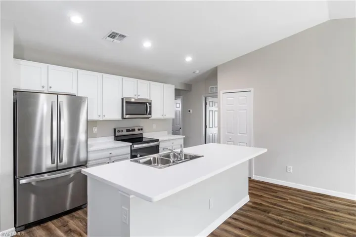 Kitchen with a center island with sink, stainless steel appliances, vaulted ceiling, and sink