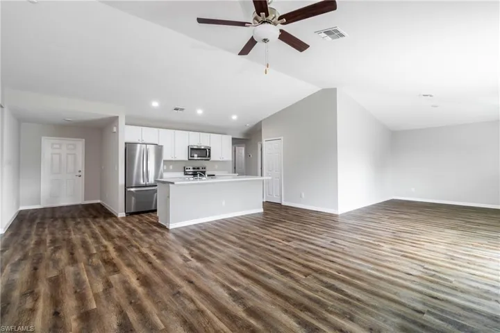 Unfurnished living room featuring ceiling fan, dark hardwood / wood-style flooring, and vaulted ceiling