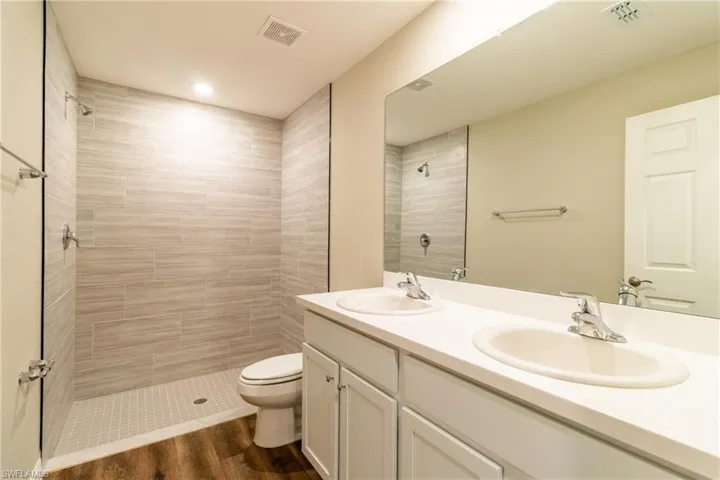 Bathroom with hardwood / wood-style flooring, vanity, toilet, and a tile shower