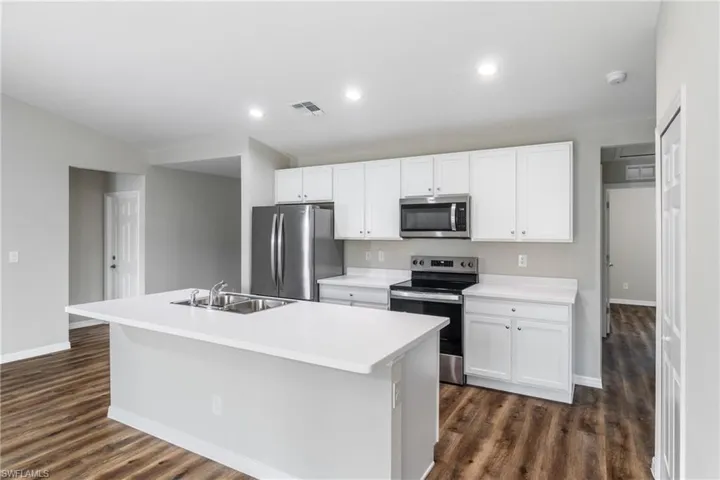 Kitchen with sink, an island with sink, stainless steel appliances, and dark hardwood / wood-style floors
