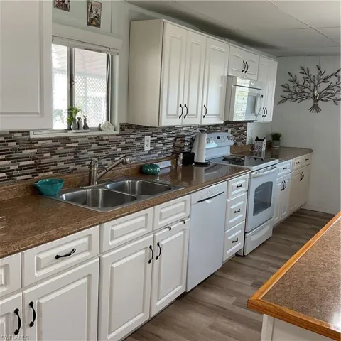 Kitchen featuring dishwashing machine, sink, white cabinetry, and range