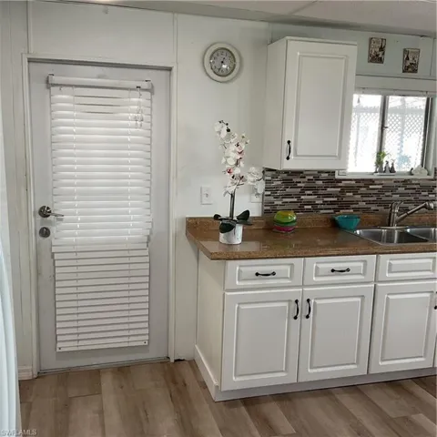 Kitchen with backsplash, light hardwood / wood-style floors, sink, and white cabinets