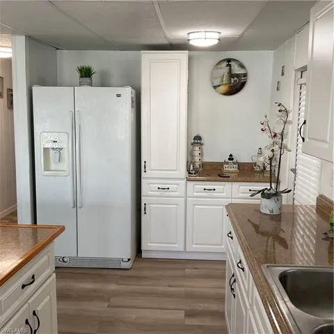 Kitchen with white cabinetry, light wood-type flooring, sink, and refrigerator