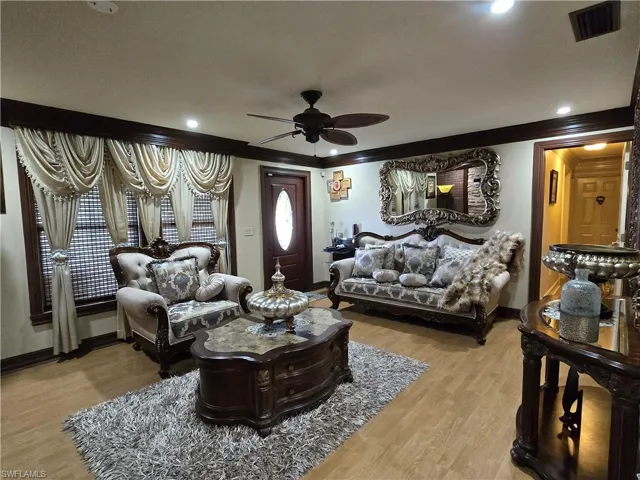 Living room featuring wood-type flooring, ornamental molding, and ceiling fan