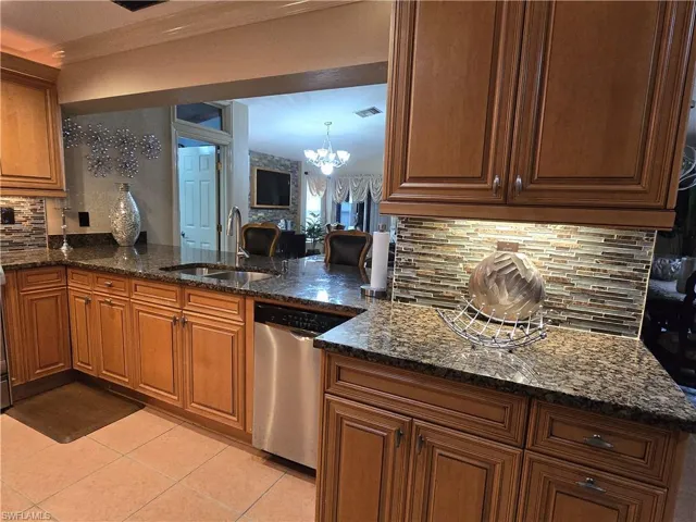 Kitchen featuring dark stone counters, stainless steel dishwasher, an inviting chandelier, backsplash, and sink