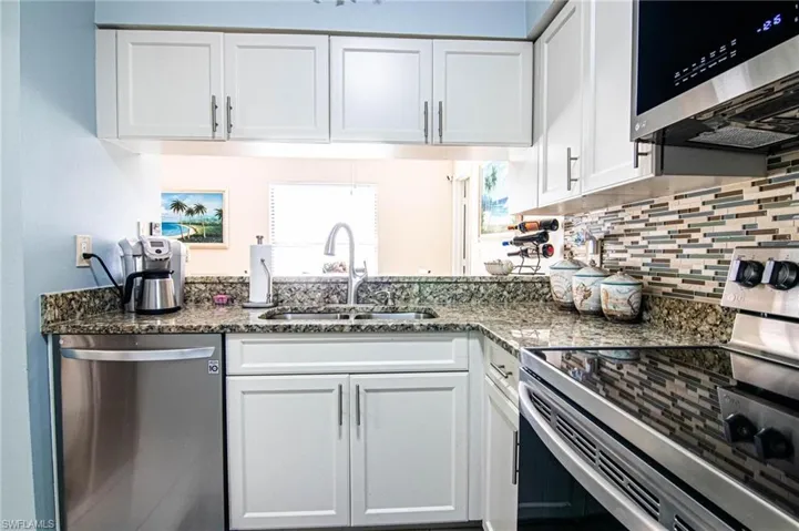Kitchen with appliances with stainless steel finishes, backsplash, dark stone counters, sink, and white cabinetry