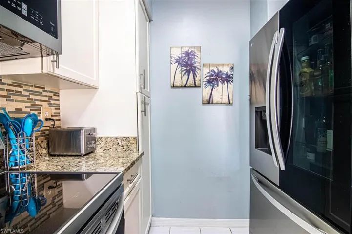Kitchen featuring backsplash, light stone counters, stainless steel fridge with ice dispenser, white cabinetry, and light tile patterned flooring