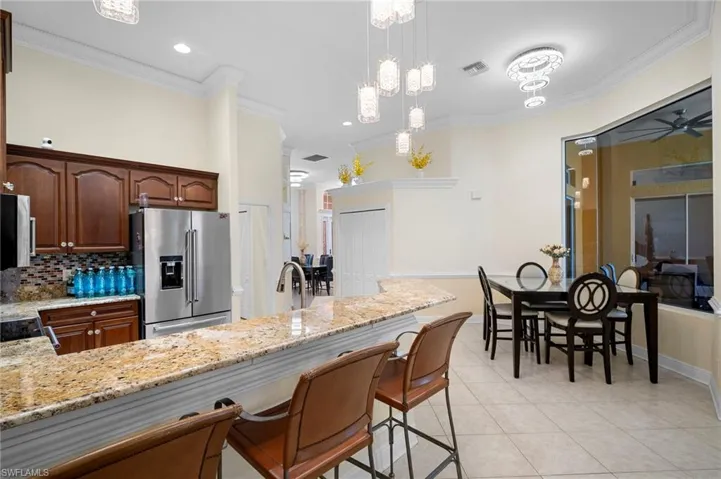 Kitchen with light stone counters, high end refrigerator, ornamental molding, hanging light fixtures, and a kitchen bar