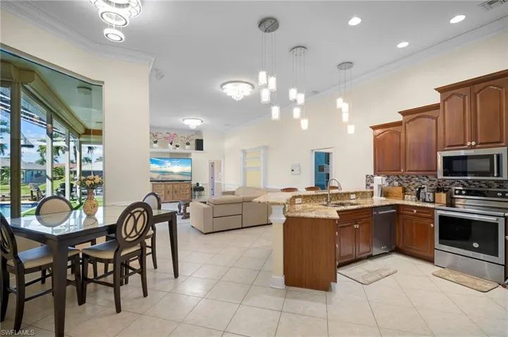 Kitchen featuring ornamental molding, hanging light fixtures, stainless steel appliances, a peninsula, and open floor plan