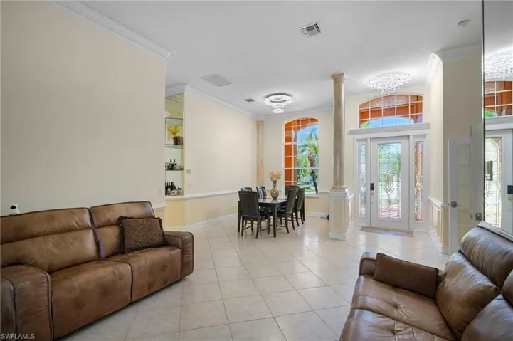 Living room with decorative columns, crown molding, and light tile patterned floors
