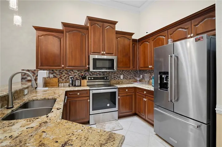 Kitchen with appliances with stainless steel finishes, ornamental molding, light stone counters, hanging light fixtures, and tasteful backsplash
