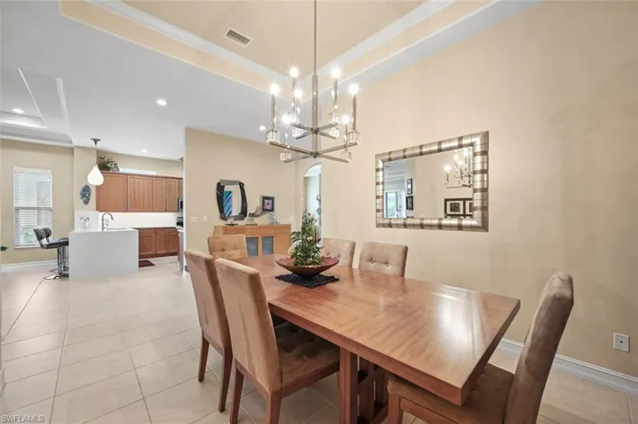 Dining area with a tray ceiling, ornamental molding, a chandelier, recessed lighting, and light tile patterned flooring