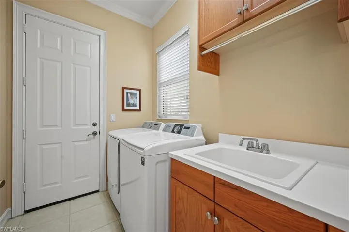 Washroom featuring washer and dryer, cabinet space, ornamental molding, and light tile patterned floors