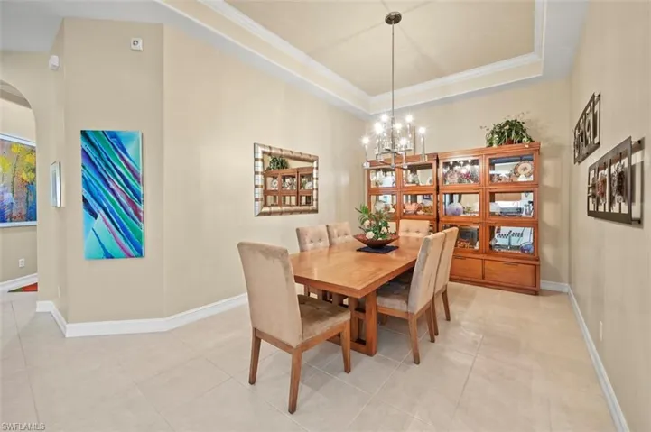 Dining space featuring a chandelier, arched walkways, light tile patterned floors, a tray ceiling, and crown molding