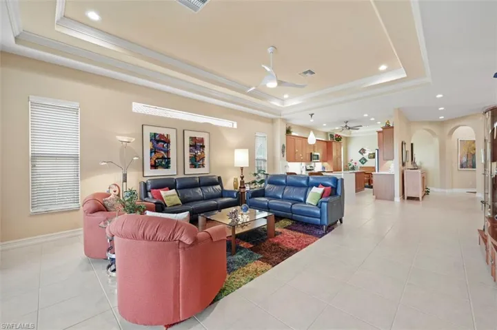 Living area with a tray ceiling, recessed lighting, arched walkways, a ceiling fan, and light tile patterned floors