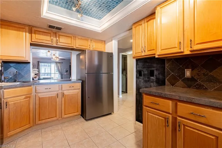 Kitchen with tasteful backsplash, stainless steel refrigerator, crown molding, and light tile patterned flooring
