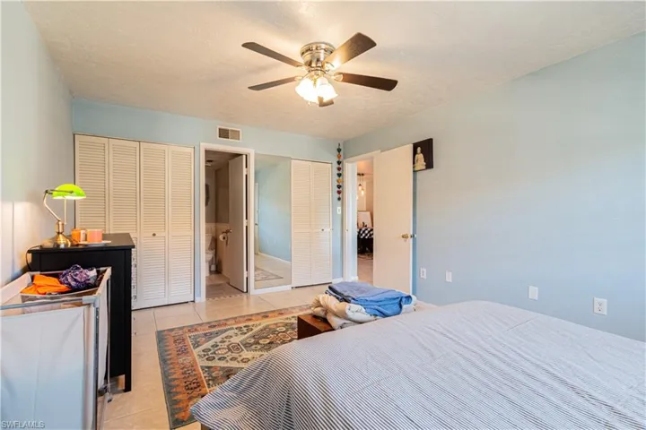 Bedroom featuring ensuite bath, ceiling fan, light tile patterned flooring, and a textured ceiling