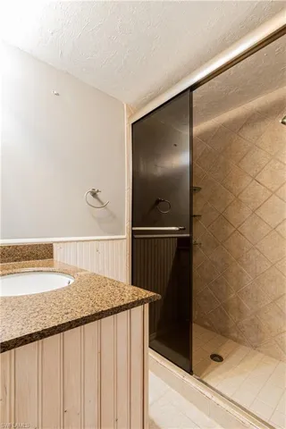 Bathroom with a tile shower, a textured ceiling, wood walls, and sink