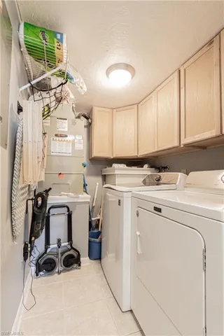 Clothes washing area with light tile patterned floors, cabinets, a textured ceiling, and independent washer and dryer