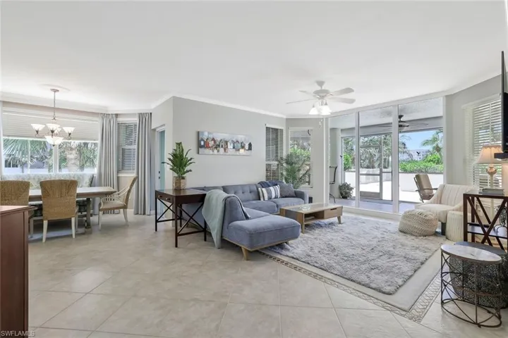 Living area with ornamental molding, a chandelier, ceiling fan, light tile patterned floors, and plenty of natural light