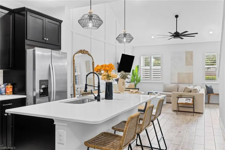 Open-concept living space featuring a kitchen island with a built-in sink, white countertops, black cabinetry, and a full-size stainless steel refrigerator