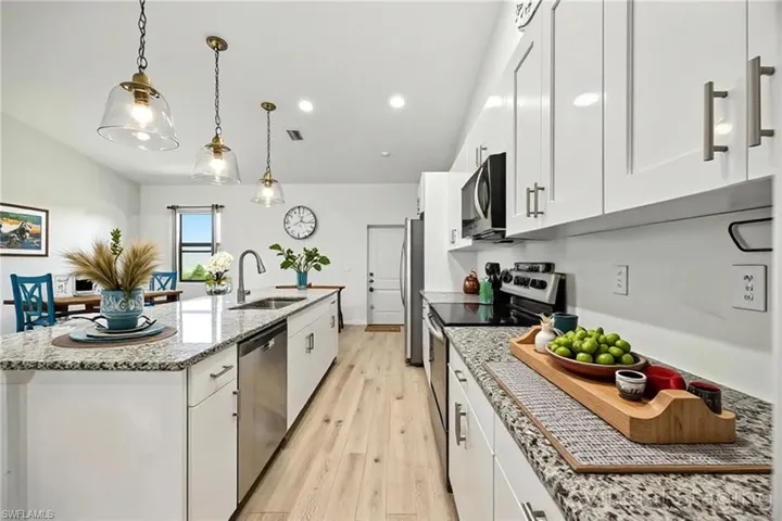 Kitchen featuring appliances with stainless steel finishes, light wood finished floors, light stone countertops, and white cabinets