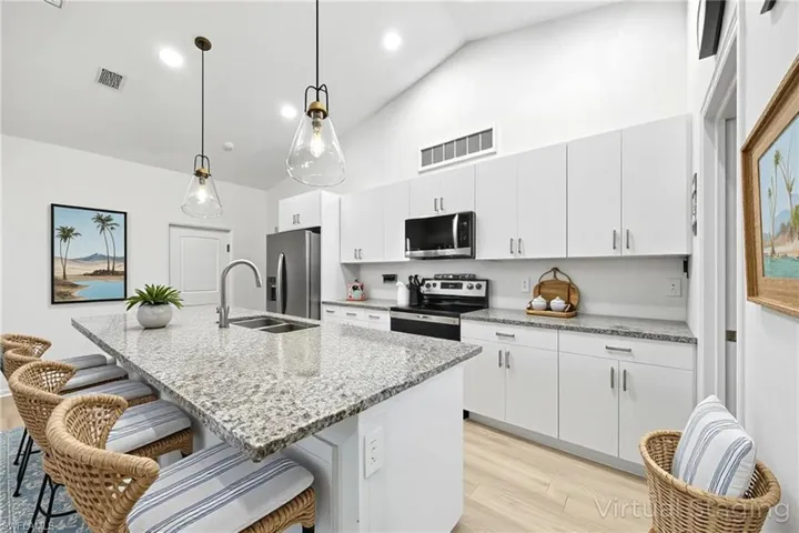 Kitchen with a breakfast bar, light wood-type flooring, light stone counters, stainless steel appliances, and high vaulted ceiling