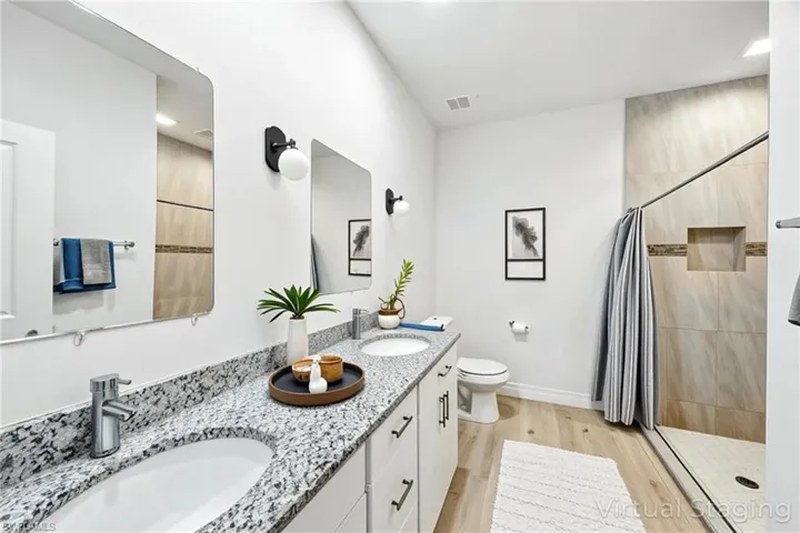 Bathroom featuring light wood-style flooring, a stall shower, and double vanity