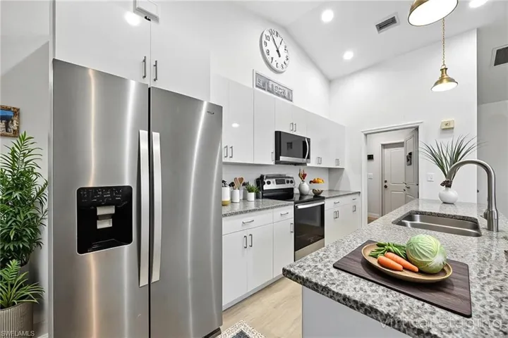 Kitchen with appliances with stainless steel finishes, light stone countertops, high vaulted ceiling, and light wood-style floors