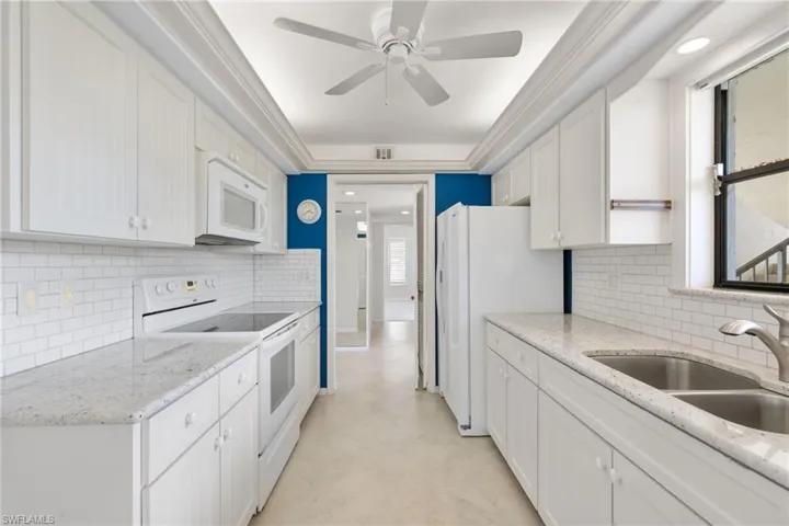 Kitchen with white appliances, light stone countertops, white cabinetry, decorative backsplash, and a ceiling fan