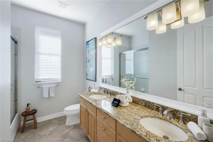 Full bathroom with double vanity, combined bath / shower with glass door, light tile patterned floors, and hanging lights