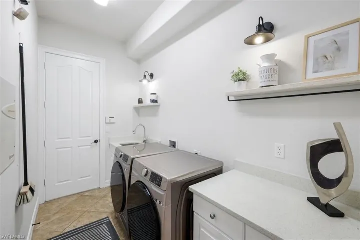 Laundry area with washing machine and clothes dryer, light tile patterned floors, and cabinet space