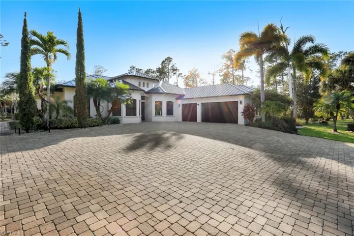 View of front of property featuring stucco siding, a garage, driveway, and a metal roof