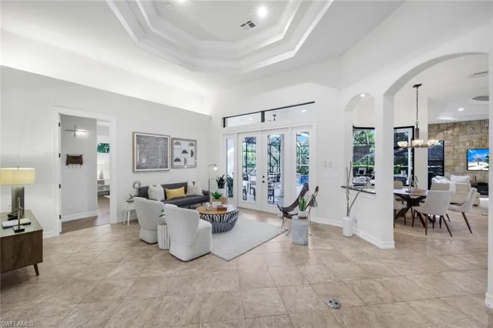 Living room with a raised ceiling, suspended lighting, arched walkways, and french doors