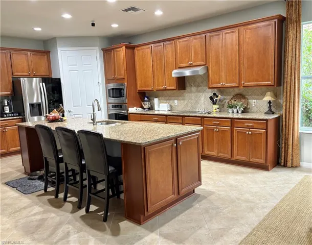 Kitchen featuring light stone countertops, appliances with stainless steel finishes, a kitchen bar, a kitchen island with sink, and sink