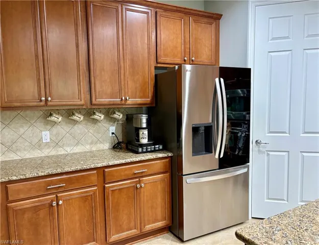 Kitchen featuring stainless steel refrigerator with ice dispenser, tasteful backsplash, light stone counters, and light tile patterned flooring