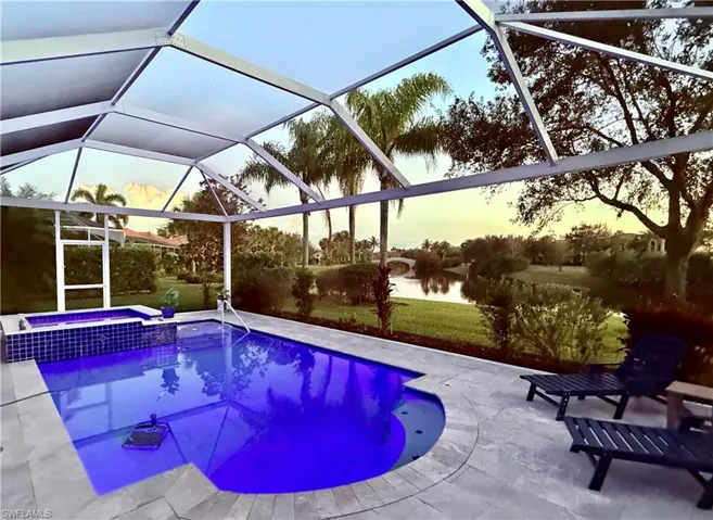 Pool at dusk with a lanai, a patio area, a water view, and an in ground hot tub