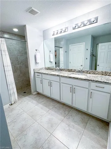 Bathroom with a textured ceiling, tile patterned flooring, walk in shower, and dual bowl vanity